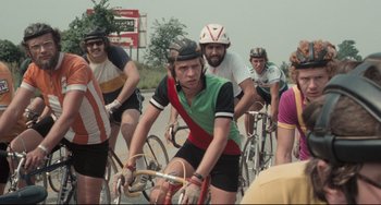Movie still from “Breaking Away” (1979), directed by Peter Yates – A group of people riding bikes down a street; Medium shot, Over the shoulder angle
