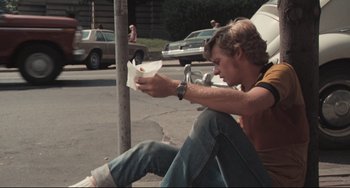 Movie still from “Breaking Away” (1979), directed by Peter Yates – A man sitting on the side of the road eating a hot dog; Medium shot, Low angle