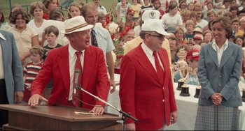 Movie still from “Breaking Away” (1979), directed by Peter Yates – Two men in red jackets and white hats standing at a podium; Medium shot, Over the shoulder angle