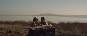 Movie still from “Breathe” (2014), directed by Mélanie Laurent – Two women sitting on a bench near a body of water; Wide shot, High angle