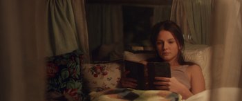 Movie still from “Breathe” (2014), directed by Mélanie Laurent – A woman sitting on a bed reading a book; Medium shot, High angle