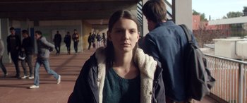 Movie still from “Breathe” (2014), directed by Mélanie Laurent – A young woman standing in a hallway with other people in the background; Medium shot, Over the shoulder angle