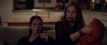 Movie still from “Breathe” (2014), directed by Mélanie Laurent – Two women sitting on a couch eating pizza; Medium shot, Over the shoulder angle