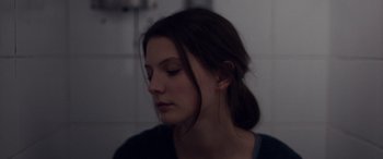 Movie still from “Breathe” (2014), directed by Mélanie Laurent – A young woman with her eyes closed in a dark room; Close Up shot, Over the shoulder angle