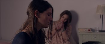 Two young women sitting in a room , one of which is praying