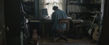 Movie still from “Breathe In” (2013), directed by Drake Doremus – A man sitting at a computer desk in front of a computer; Wide shot, High angle