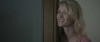 Movie still from “Breathe In” (2013), directed by Drake Doremus – A beautiful young blonde woman standing next to a wooden door; Close Up shot, Over the shoulder angle