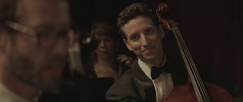 Movie still from “Breathe In” (2013), directed by Drake Doremus – A man in a suit and bow tie holding a violin; Close Up shot, Over the shoulder angle
