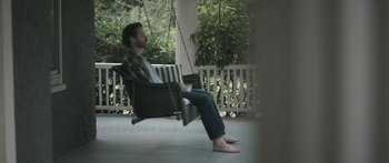 Movie still from “Breathe In” (2013), directed by Drake Doremus – A man sitting on a porch swing on a porch; Wide shot, High angle