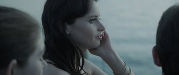 Movie still from “Breathe In” (2013), directed by Drake Doremus – A beautiful young lady sitting in front of a body of water talking on a cell phone; Close Up shot, High angle