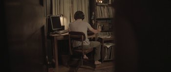 Movie still from “Breathe In” (2013), directed by Drake Doremus – A man sitting at a desk in front of a computer; Wide shot, High angle