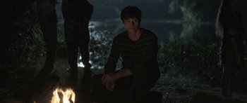 Movie still from “Breathe In” (2013), directed by Drake Doremus – A man sitting on the ground next to a fire pit; Medium shot, Over the shoulder angle