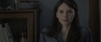 Movie still from “Breathe In” (2013), directed by Drake Doremus – A woman sitting in front of a wooden cabinet; Close Up shot, Over the shoulder angle