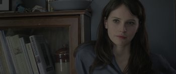 Movie still from “Breathe In” (2013), directed by Drake Doremus – A woman sitting in front of a wooden cabinet; Close Up shot, Over the shoulder angle