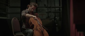 Movie still from “Breathe In” (2013), directed by Drake Doremus – A man is playing the cello in a dark room; Medium shot, High angle