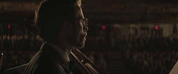 Movie still from “Breathe In” (2013), directed by Drake Doremus – A person wearing a suit and glasses; Close Up shot, Over the shoulder angle