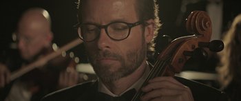 Movie still from “Breathe In” (2013), directed by Drake Doremus – A person wearing glasses and holding a violin; Close Up shot, Low angle