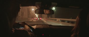 Movie still from “Breathe In” (2013), directed by Drake Doremus – A person is seen in the rear view mirror of a car at night; Close Up shot, Over the shoulder angle