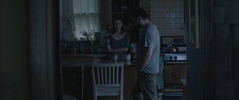 Movie still from “Breathe In” (2013), directed by Drake Doremus – A man and a woman standing in a dark kitchen; Medium shot, Over the shoulder angle