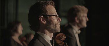 Movie still from “Breathe In” (2013), directed by Drake Doremus – A man in a suit and tie holding a violin; Close Up shot, Over the shoulder angle