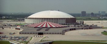 Movie still from “Brewster McCloud” (1970), directed by Robert Altman – An arena with a red and white striped tent on top of it; Extreme Wide shot, High angle