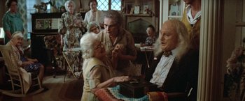 Movie still from “Brewster McCloud” (1970), directed by Robert Altman – An older woman holding a box in front of a group of people; Medium shot, High angle