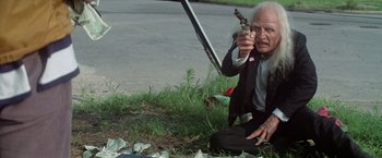 Movie still from “Brewster McCloud” (1970), directed by Robert Altman – An old man in a suit and tie holding a gun; Medium shot, Low angle
