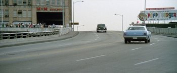 Movie still from “Brewster McCloud” (1970), directed by Robert Altman – A car driving down a street next to a street light; Extreme Wide shot, High angle