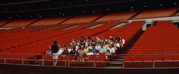 Movie still from “Brewster McCloud” (1970), directed by Robert Altman – A group of people sitting in the stands of a stadium; Extreme Wide shot, High angle