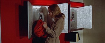 Movie still from “Brewster McCloud” (1970), directed by Robert Altman – A woman in a trench coat is looking at a red bag; Medium shot, Low angle