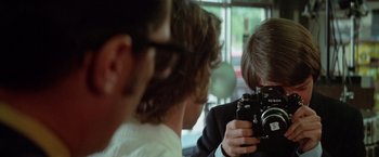 Movie still from “Brewster McCloud” (1970), directed by Robert Altman – A man taking a picture of another man with a camera; Close Up shot, Over the shoulder angle