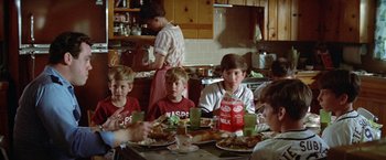 Movie still from “Brewster McCloud” (1970), directed by Robert Altman – A group of people sitting at a table with plates of food on it; Medium shot, Over the shoulder angle