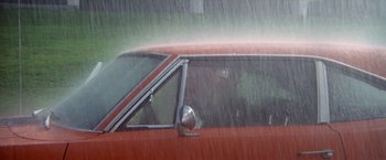 Movie still from “Brewster McCloud” (1970), directed by Robert Altman – A red car is driving in the rain; Wide shot, High angle
