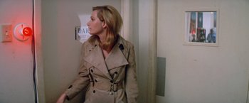 Movie still from “Brewster McCloud” (1970), directed by Robert Altman – A woman wearing a trench coat standing next to a door; Medium shot, Over the shoulder angle