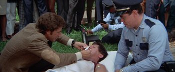 Movie still from “Brewster McCloud” (1970), directed by Robert Altman – A group of men standing around a man on the ground; Medium shot, High angle