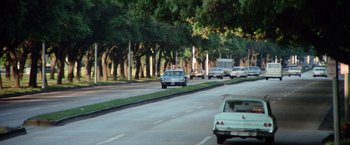 Movie still from “Brewster McCloud” (1970), directed by Robert Altman – Cars driving down a street lined with tall trees; Extreme Wide shot, Over the shoulder angle