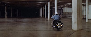 Movie still from “Brewster McCloud” (1970), directed by Robert Altman – A man riding a motorcycle in a large building; Extreme Wide shot, High angle