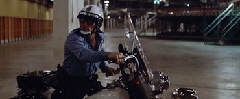 Movie still from “Brewster McCloud” (1970), directed by Robert Altman – A man riding on the back of a motorcycle at night; Medium shot, Low angle