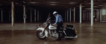 Movie still from “Brewster McCloud” (1970), directed by Robert Altman – A police officer sitting on top of a white motorcycle; Wide shot, High angle