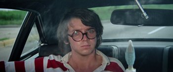 Movie still from “Brewster McCloud” (1970), directed by Robert Altman – A young man wearing glasses sitting in the back of a car; Close Up shot, Over the shoulder angle