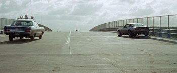 Movie still from “Brewster McCloud” (1970), directed by Robert Altman – A car driving down a road next to an overpass; Extreme Wide shot, Low angle