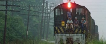 Movie still from “Brewster McCloud” (1970), directed by Robert Altman – Three people are sitting on the back of a train car; Extreme Wide shot, Low angle