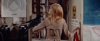 Movie still from “Brewster McCloud” (1970), directed by Robert Altman – A woman in a trench coat holding a black bird; Medium shot, Over the shoulder angle