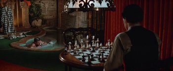 Movie still from “Brewster McCloud” (1970), directed by Robert Altman – A person is playing a game of chess on a table; Wide shot, High angle