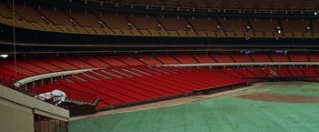 Movie still from “Brewster McCloud” (1970), directed by Robert Altman – An empty baseball stadium with red seats and a green field; Extreme Wide shot, High angle