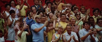 Movie still from “Brewster McCloud” (1970), directed by Robert Altman – A large group of men and women clapping in front of a crowd; Wide shot, High angle