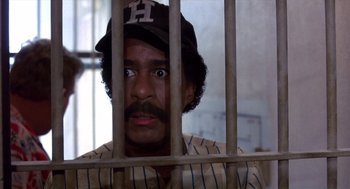 Movie still from “Brewster's Millions” (1985), directed by Walter Hill – A man in a baseball cap looking through a fence; Close Up shot, Low angle