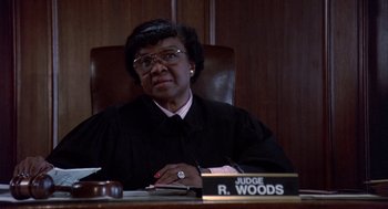 Movie still from “Brewster's Millions” (1985), directed by Walter Hill – A judge sitting at a table in a courtroom; Medium shot, High angle