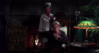 Movie still from “Brewster's Millions” (1985), directed by Walter Hill – An older man and woman sitting next to each other in front of a fireplace; Medium shot, High angle