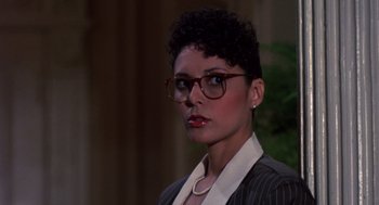 Movie still from “Brewster's Millions” (1985), directed by Walter Hill – A woman wearing glasses and a suit and necklace; Close Up shot, Over the shoulder angle